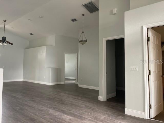 unfurnished living room featuring visible vents, baseboards, dark wood-style floors, ceiling fan, and high vaulted ceiling