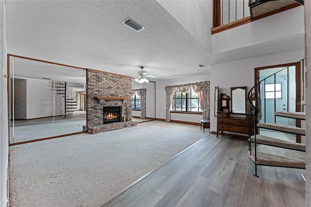 unfurnished living room with ceiling fan, visible vents, baseboards, stairs, and a brick fireplace