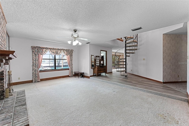 unfurnished living room with ceiling fan, carpet flooring, visible vents, stairs, and a brick fireplace