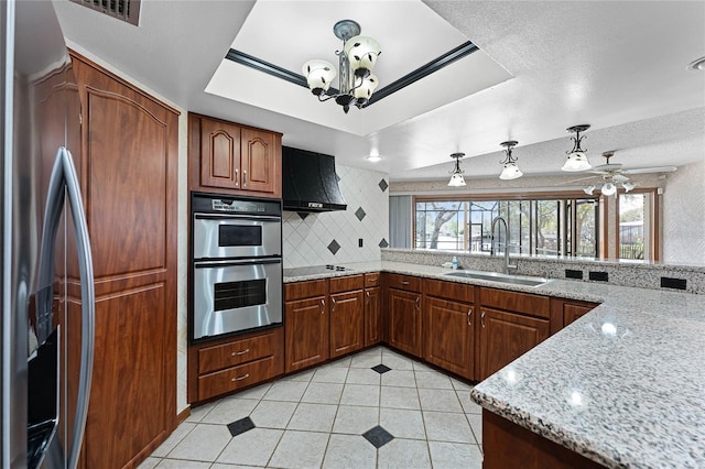 kitchen featuring stainless steel double oven, built in refrigerator, a sink, range hood, and a tray ceiling