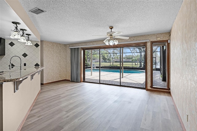 interior space featuring a textured ceiling, visible vents, baseboards, light wood-style floors, and wallpapered walls