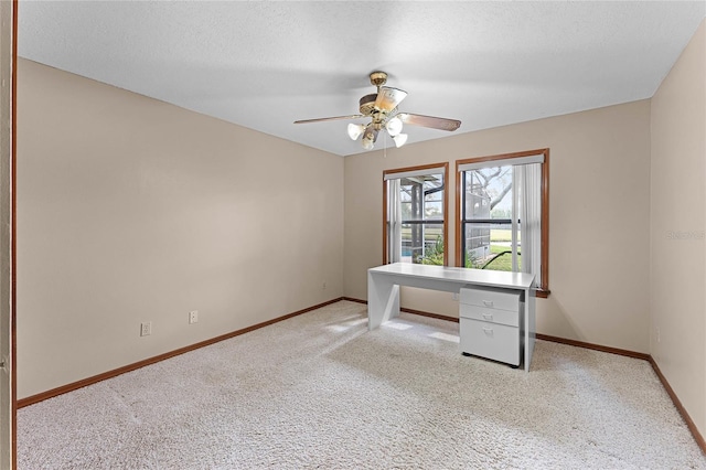 unfurnished office with a textured ceiling, carpet flooring, a ceiling fan, and baseboards