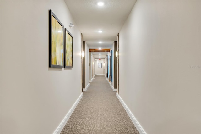 hallway featuring light colored carpet and baseboards