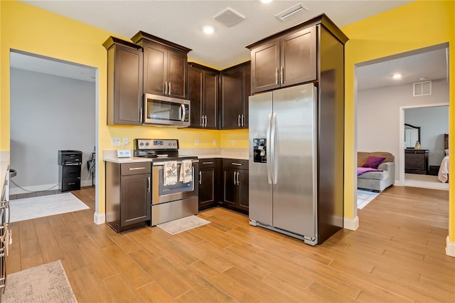 kitchen with dark brown cabinetry, visible vents, light wood-style flooring, stainless steel appliances, and light countertops