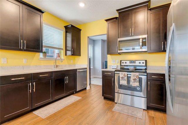 kitchen featuring dark brown cabinetry, stainless steel appliances, a sink, light countertops, and light wood finished floors