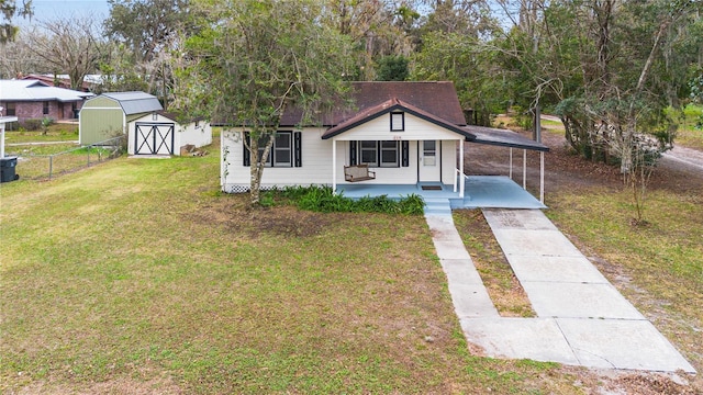 bungalow-style house with an attached carport, an outdoor structure, a shed, a front lawn, and a porch