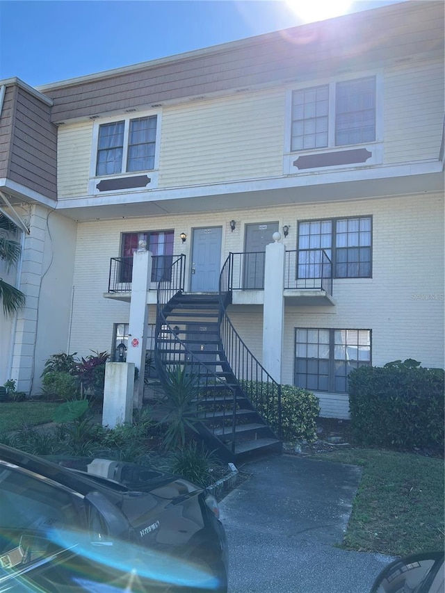 view of front of house featuring stairs, brick siding, mansard roof, and a porch