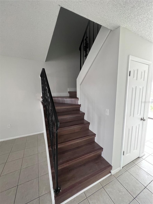 stairway with tile patterned flooring, baseboards, and a textured ceiling