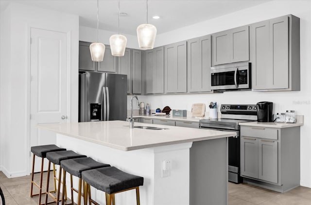 kitchen featuring stainless steel appliances, light countertops, gray cabinetry, a sink, and a kitchen bar