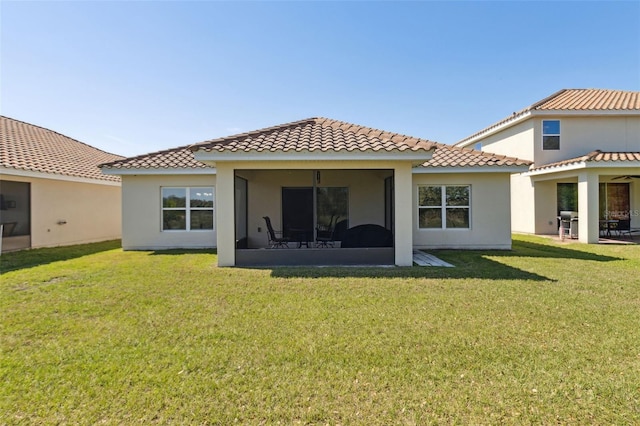 back of property with a yard, a tiled roof, a sunroom, and stucco siding