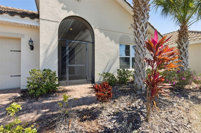 view of exterior entry featuring a garage, a tile roof, and stucco siding