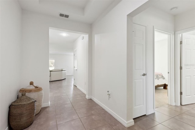 hall featuring light tile patterned flooring, visible vents, and baseboards