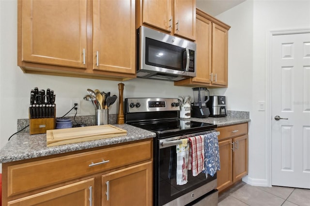 kitchen with light tile patterned floors, stone counters, appliances with stainless steel finishes, and brown cabinets