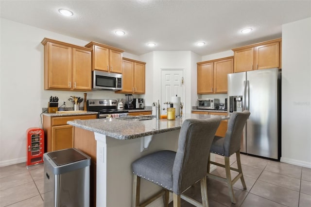 kitchen with light tile patterned floors, stainless steel appliances, a kitchen island with sink, and a kitchen breakfast bar