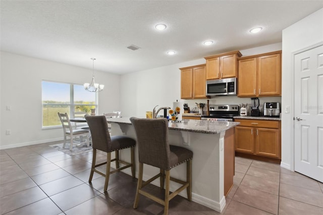 kitchen with a center island with sink, light tile patterned floors, visible vents, appliances with stainless steel finishes, and a kitchen breakfast bar