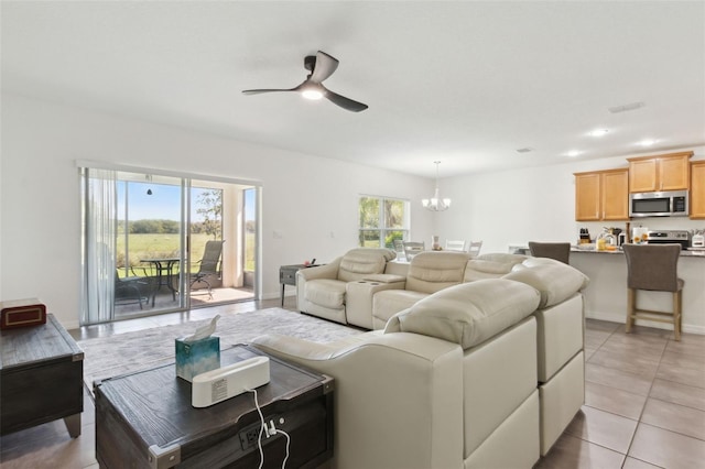 living area with ceiling fan with notable chandelier, a healthy amount of sunlight, baseboards, and light tile patterned flooring