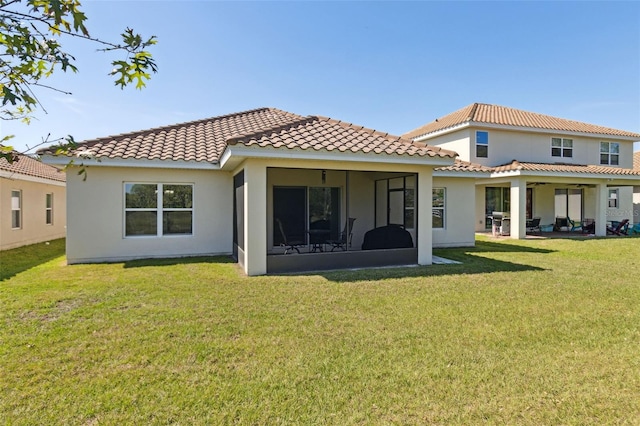 rear view of property featuring a sunroom, a tile roof, a lawn, and stucco siding