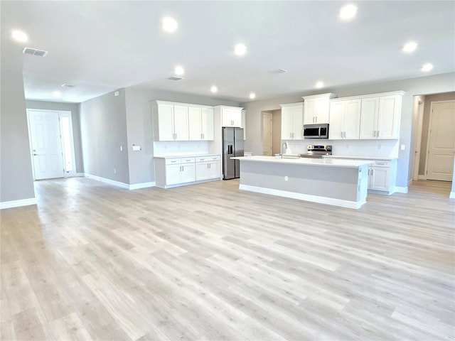 kitchen featuring baseboards, an island with sink, appliances with stainless steel finishes, open floor plan, and light countertops