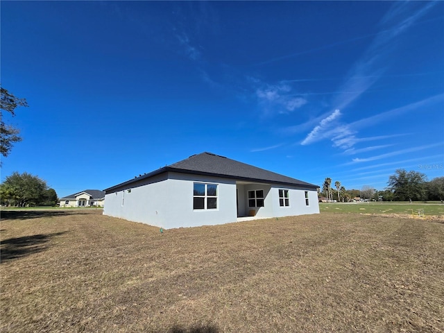 rear view of property featuring a lawn and stucco siding