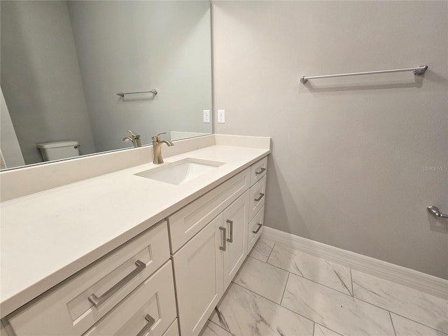 bathroom with toilet, marble finish floor, vanity, and baseboards