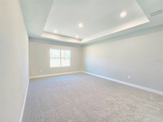 carpeted empty room with visible vents, baseboards, a raised ceiling, and recessed lighting