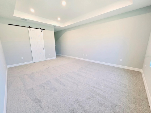 unfurnished bedroom featuring a tray ceiling, recessed lighting, light colored carpet, a barn door, and baseboards