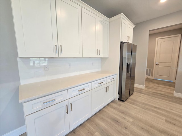 kitchen with light wood-type flooring, stainless steel fridge, white cabinets, and decorative backsplash