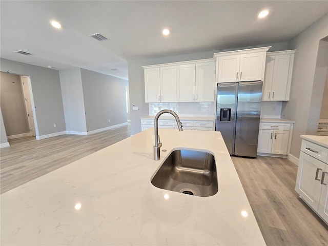 kitchen featuring stainless steel refrigerator with ice dispenser, a sink, visible vents, and white cabinets