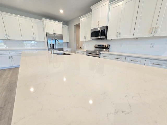 kitchen featuring appliances with stainless steel finishes, white cabinetry, a sink, and tasteful backsplash