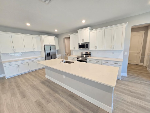 kitchen featuring light wood-style flooring, stainless steel appliances, a sink, white cabinetry, and an island with sink