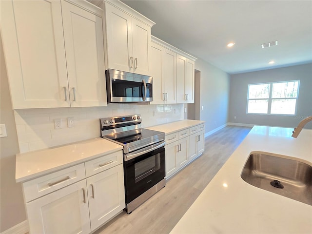 kitchen featuring stainless steel appliances, a sink, visible vents, white cabinets, and tasteful backsplash