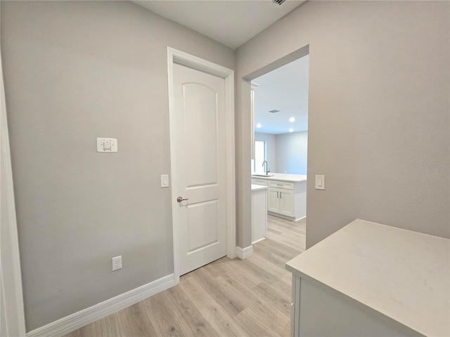 corridor featuring light wood finished floors, baseboards, and a sink