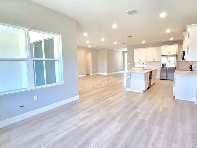 kitchen featuring visible vents, open floor plan, a kitchen island with sink, stainless steel appliances, and light countertops