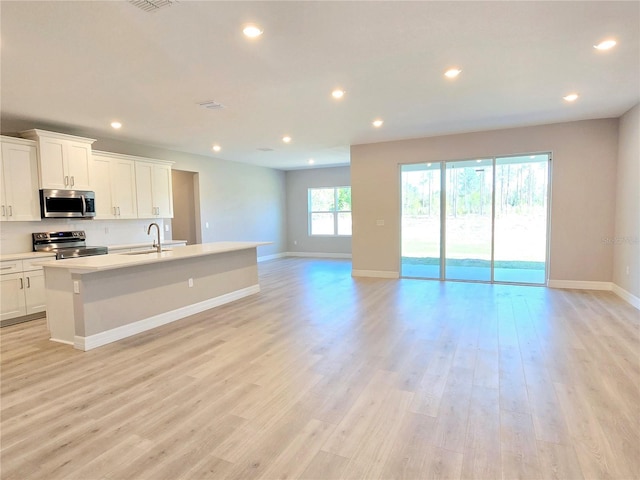 kitchen with an island with sink, light wood-style flooring, open floor plan, stainless steel appliances, and recessed lighting