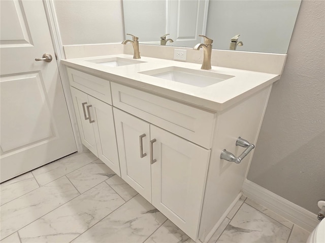 bathroom featuring double vanity, marble finish floor, baseboards, and a sink