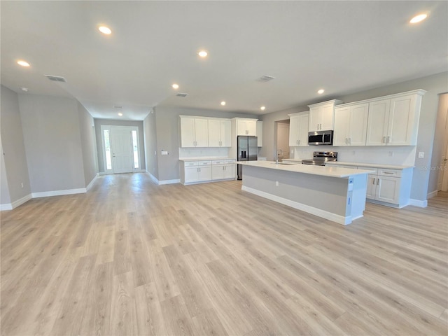 kitchen featuring light wood-style flooring, open floor plan, light countertops, appliances with stainless steel finishes, and a center island with sink