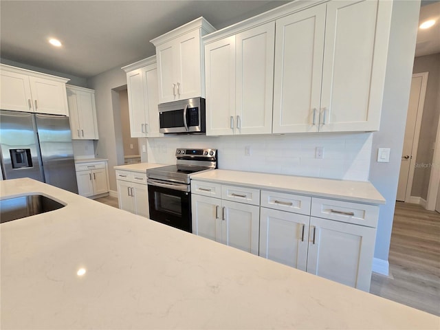 kitchen featuring stainless steel appliances, tasteful backsplash, wood finished floors, and white cabinetry