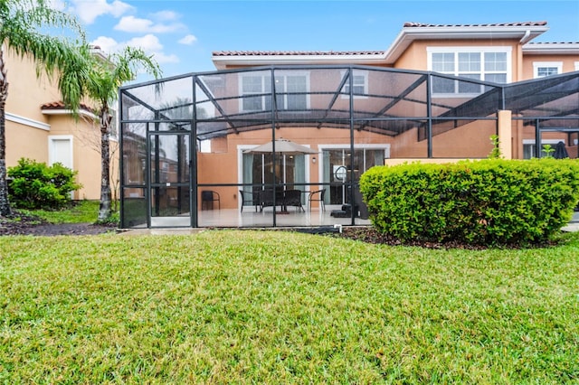 rear view of house featuring glass enclosure, a tile roof, a lawn, and stucco siding