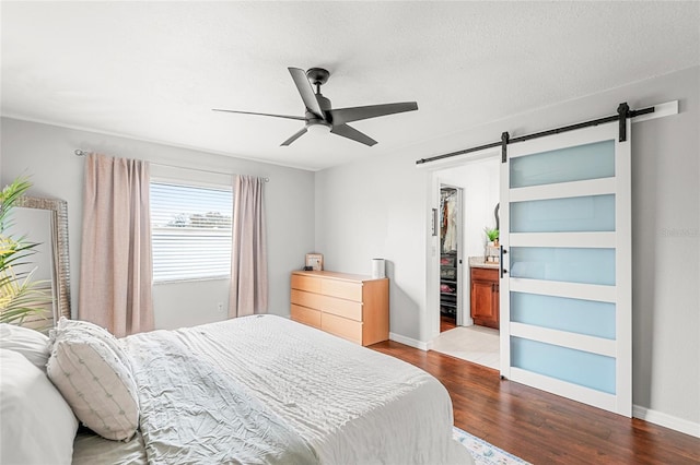 bedroom with a spacious closet, a barn door, ceiling fan, wood finished floors, and baseboards