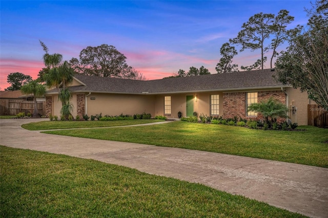 view of front of property featuring brick siding, a yard, stucco siding, a garage, and driveway