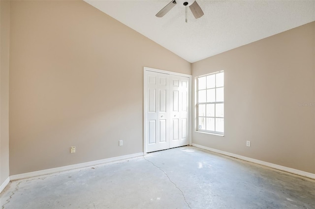 unfurnished bedroom with concrete flooring, lofted ceiling, a ceiling fan, baseboards, and a closet