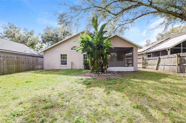 rear view of house featuring a sunroom, a fenced backyard, a yard, and stucco siding