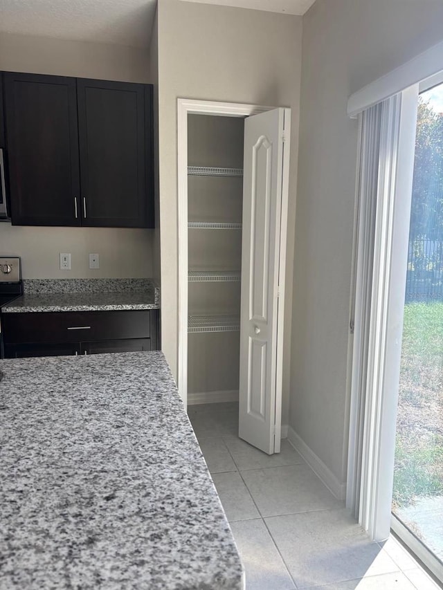 137 Willow Dr, Kissimmee, FL 34759 - kitchen featuring light tile patterned floors, dark cabinetry, light stone countertops, and baseboards