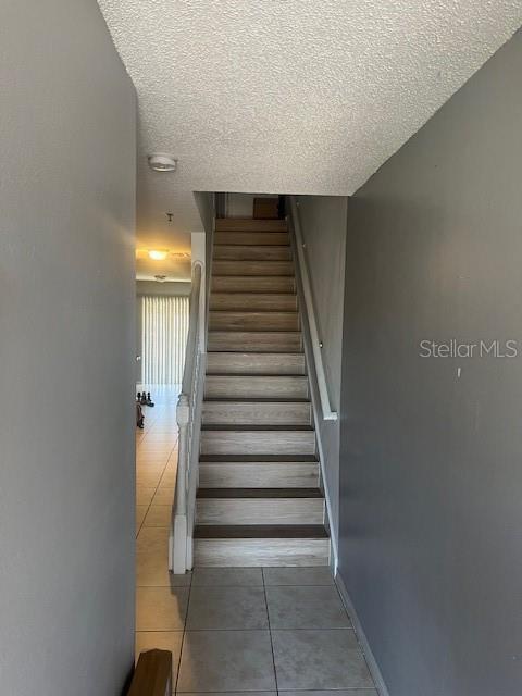 stairs with baseboards, a textured ceiling, and tile patterned floors