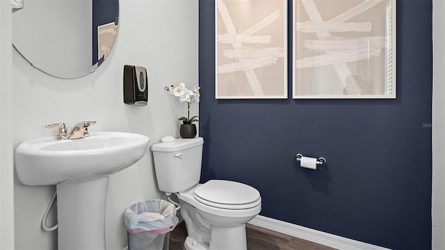 half bath with a sink, toilet, baseboards, and wood finished floors