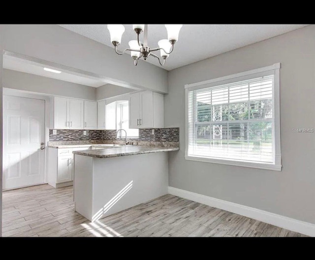 kitchen with pendant lighting, backsplash, an inviting chandelier, white cabinets, and a peninsula