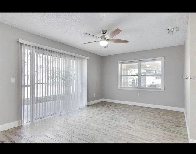 empty room with visible vents, a ceiling fan, a textured ceiling, light wood-type flooring, and baseboards