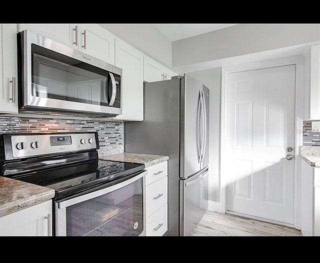 kitchen featuring stainless steel appliances, light wood-style flooring, decorative backsplash, white cabinetry, and light stone countertops