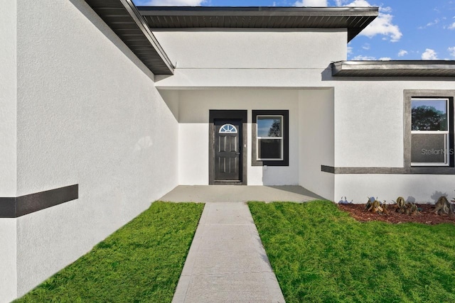 doorway to property with a lawn and stucco siding