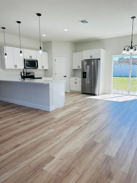 kitchen with pendant lighting, light countertops, appliances with stainless steel finishes, light wood-style floors, and white cabinetry